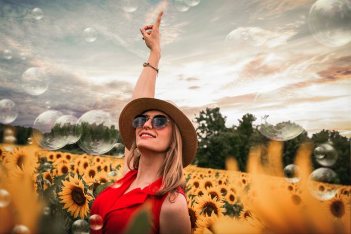 woman-surrounded-by-sunflowers-raising-hand-1261459
