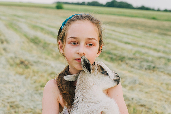 girl with baby goat on farm outdoors. Love and care. Village animals. happy child hugs goat, concept of unity of nature