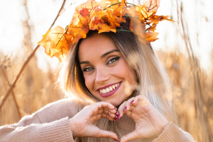attractive-young-woman-wearing-maple-leaves-tiara-making-heart-shape-with-hand